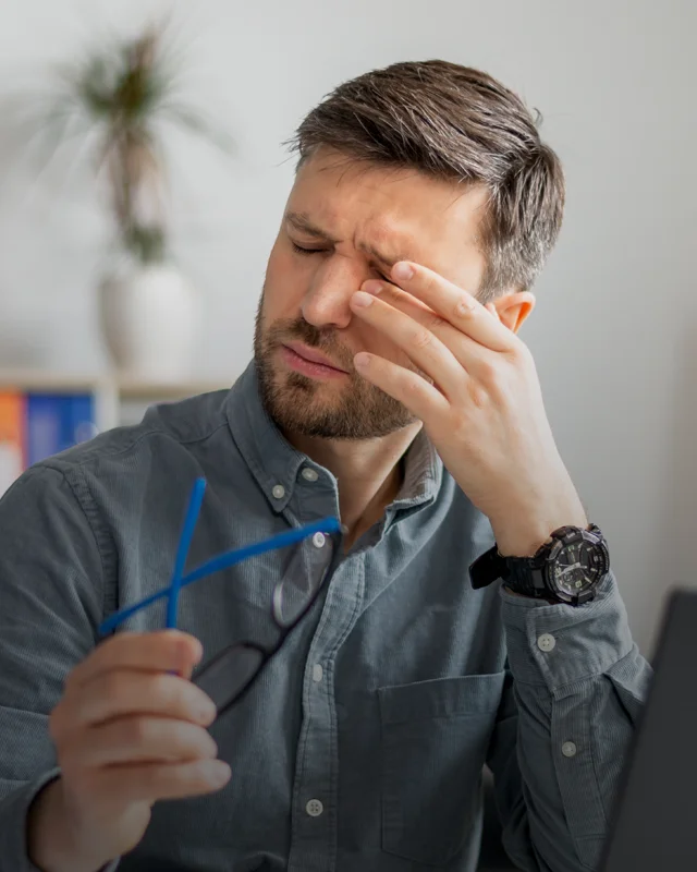 A man at a desk reaching up to rub his dry, itchy eyes