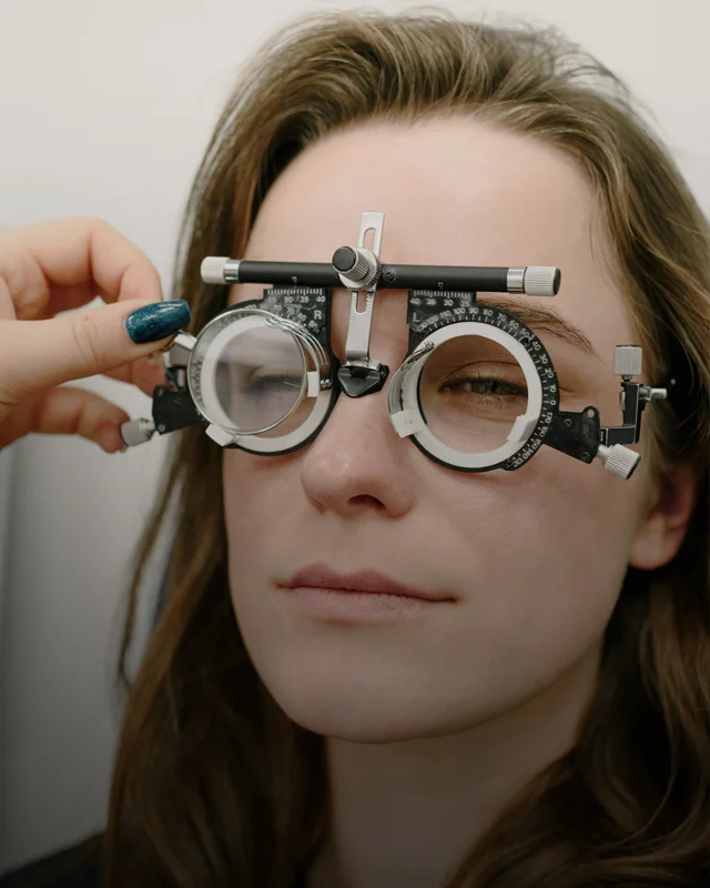 A woman looking forward at an eye chart during an eye exam while an optometrist switches lenses